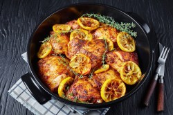 Ofenhähnchen mit Zitrone in einer gusseisernen Pfanne mit Zitronenscheiben.