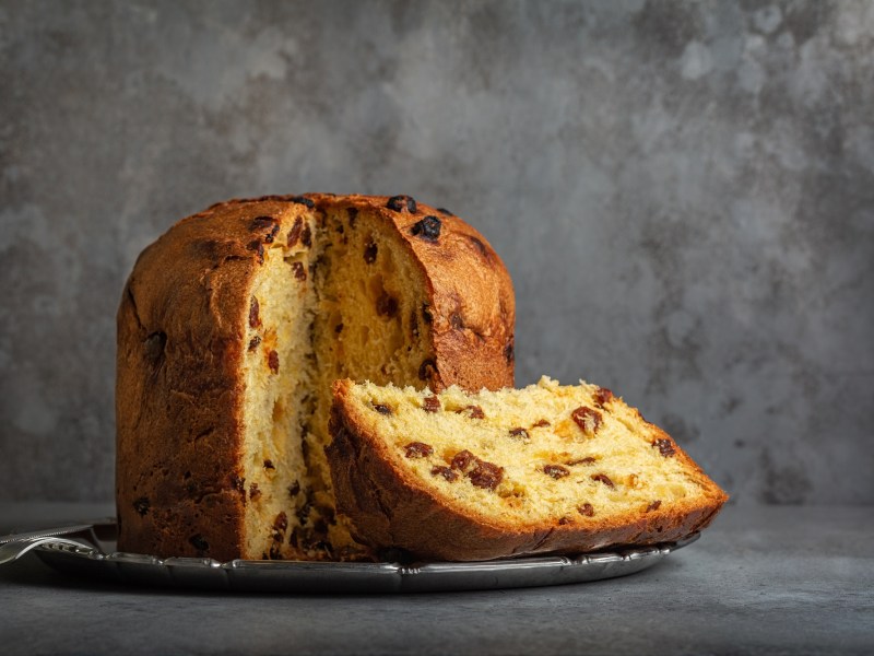 Ein angeschnittener Panettone auf einem Teller vor einem grauen Hintergrund.