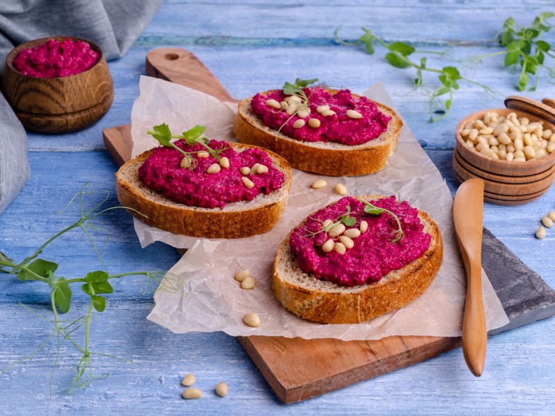 Drei Brotscheiben, mit Rote-Bete-Meerrettich-Aufstrich bestrichen und mit Pinienkernen und Erbsensprossen garniert.