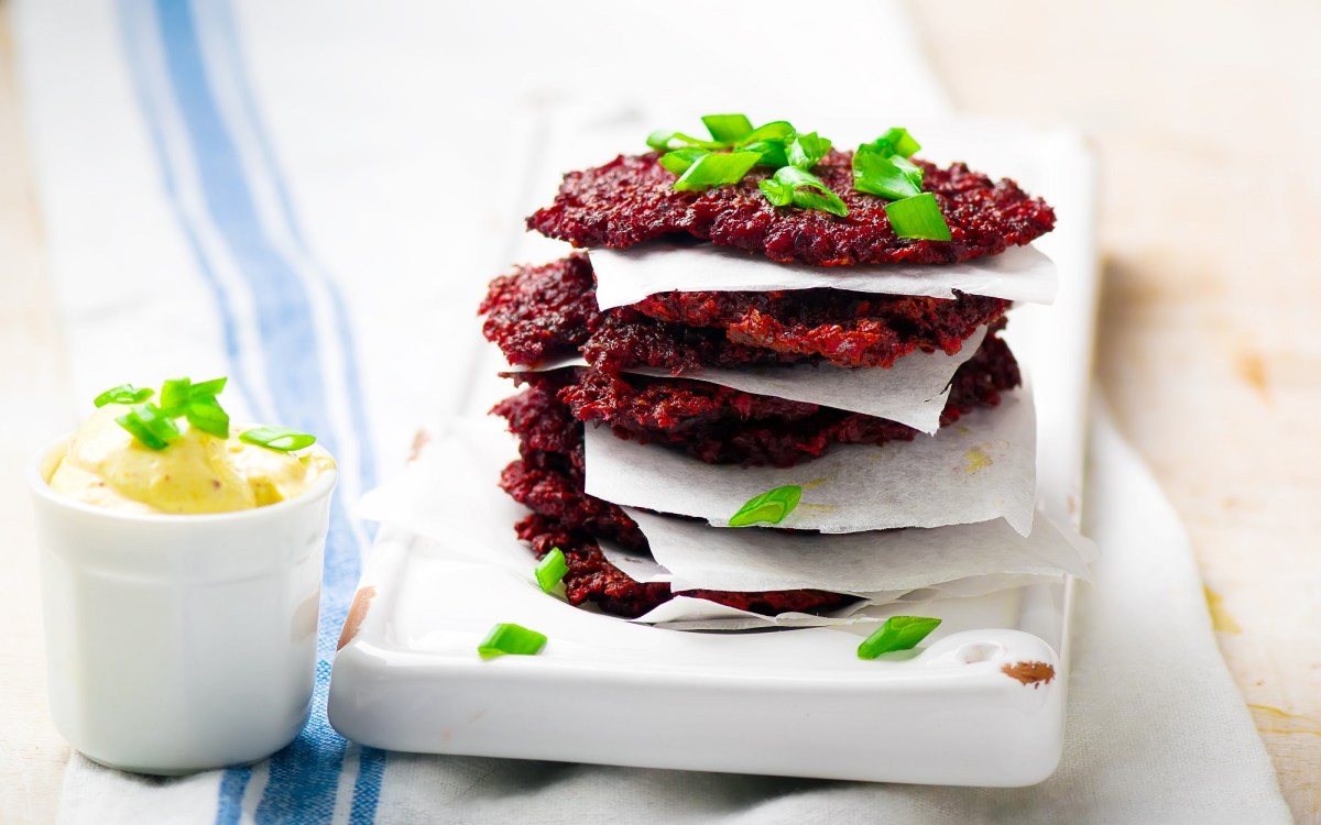 Ein Stapel Rote-Bete-Puffer auf einer weiÃŸen Unterlage, getrennt von kleinen StÃ¼cken Backpapier.