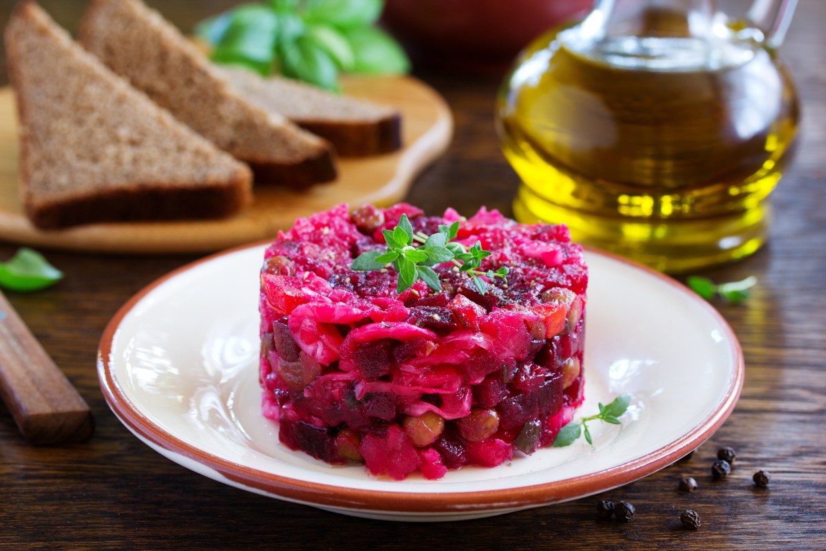 Rote-Bete-Tatar auf einem weiÃŸen Teller, dahinter eine Flasche Ã–l und Brotscheiben.