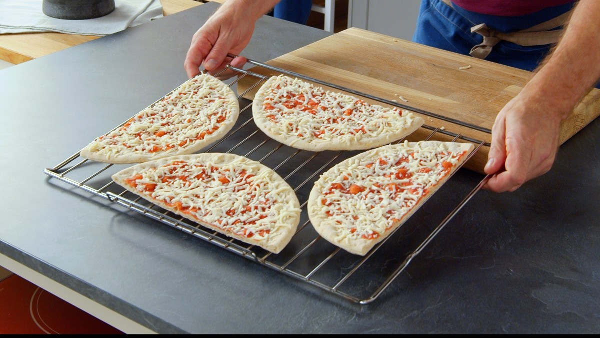 Zwei Pizzen auf einem Blech backen: Zwei Pizzen liegen angeschnitten auf einem Kuchengitter.