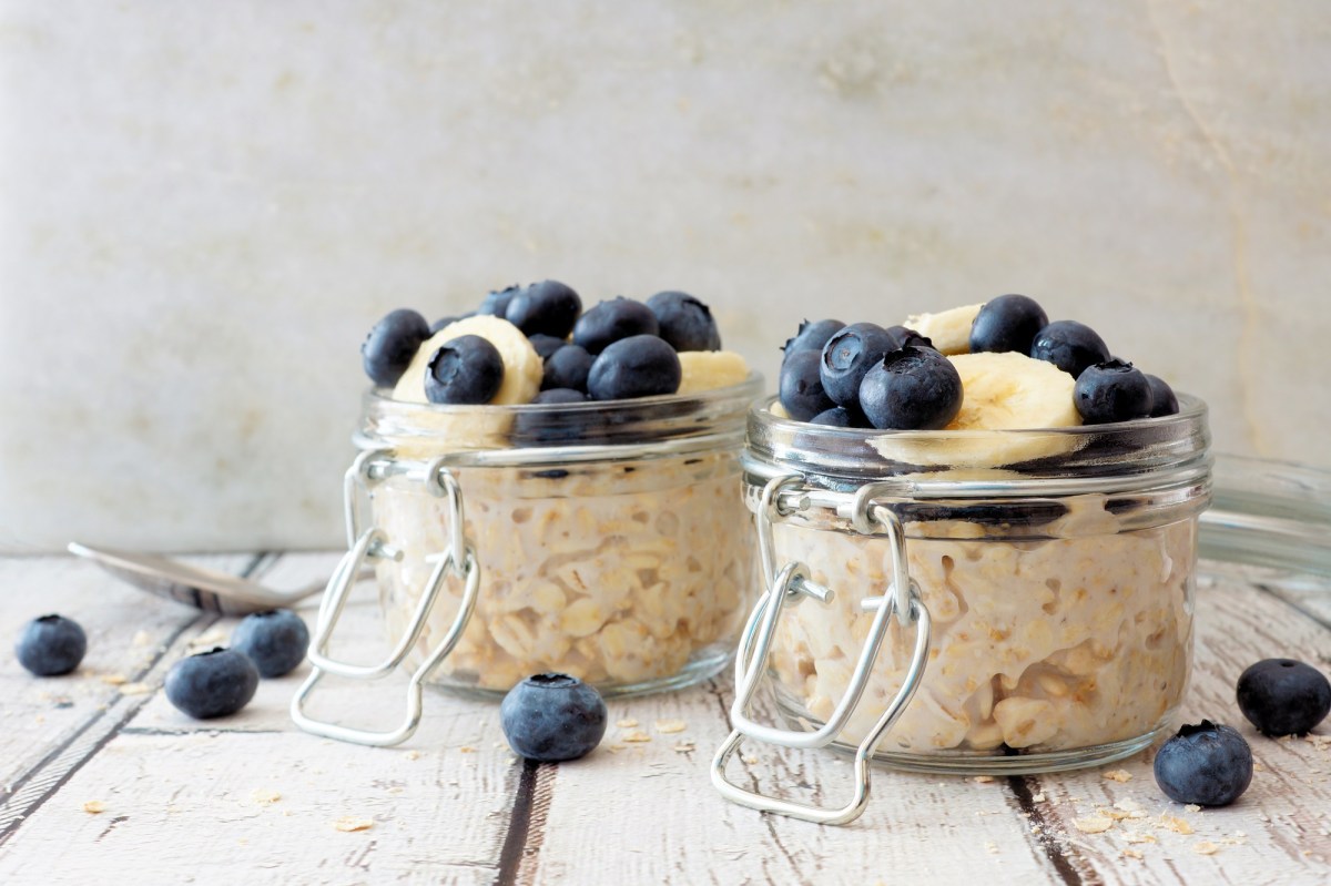 2 GlÃ¤ser Overnight Oats garniert mit Blaubeeren und Banananscheiben, drumherum liegen einige Blaubeeren.