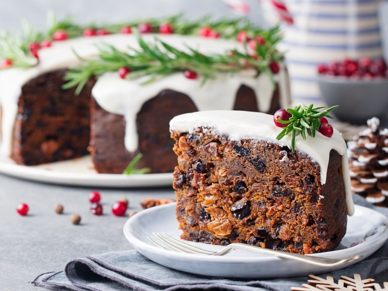 Ein StÃ¼ck Englischer Weihnachtskuchen. Im Hintergrund ist der Rest des Kuchens zu sehen.