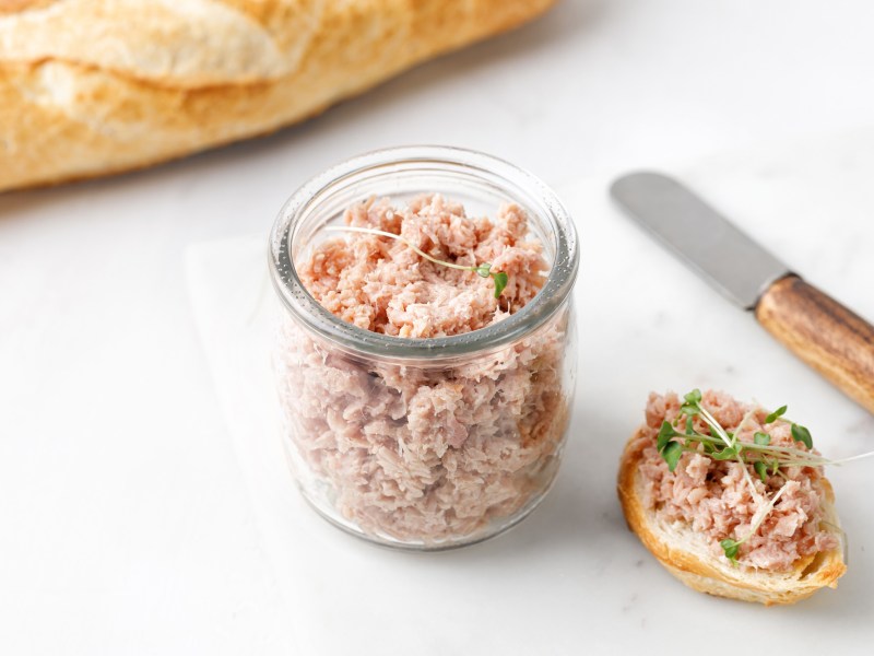 GÃ¤nse-Rillettes in einem Glas, einiges davon wurde bereits auf ein Brot gestrichen.