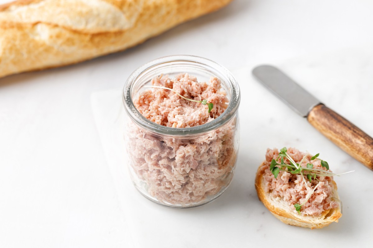 GÃ¤nse-Rillettes in einem Glas, einiges davon wurde bereits auf ein Brot gestrichen.