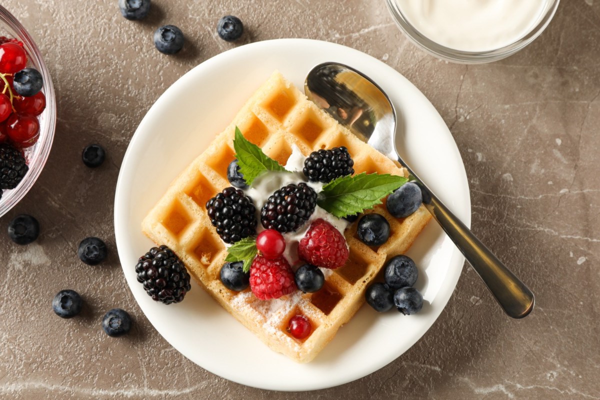 Eine Käsekuchenwaffel mit Früchten, Puderzucker und Sahne auf einem Teller in der Draufsicht.