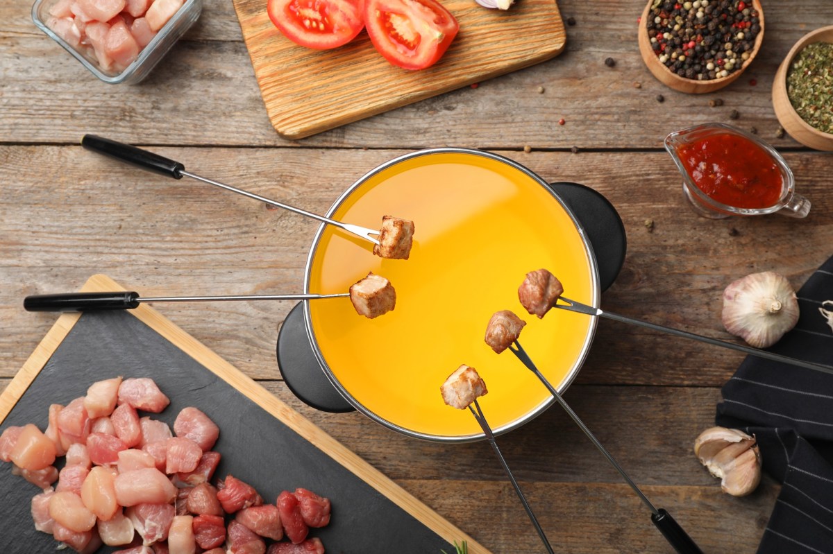 Ein Topf klassisches Fleischfondue, Ã¼ber dem mehrere Fleischgabeln mit StÃ¼cken hÃ¤ngen.