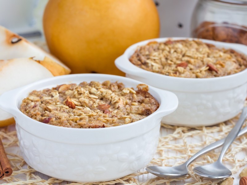 Zwei kleine Förmchen mit Ofen-Porridge. Im Hintergrund liegen frische Birnen.