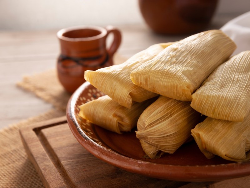 Tamales: mexikanische Mais-Teigtaschen auf einem Teller. Dahinter eine Tasse heiÃŸe Schokolade.