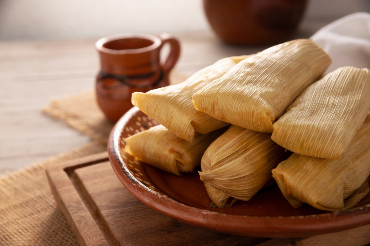 Tamales: mexikanische Mais-Teigtaschen auf einem Teller. Dahinter eine Tasse heiÃŸe Schokolade.