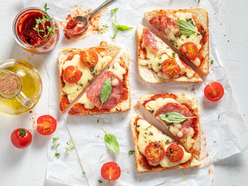 Überbackene Mozzarella-Toasts, umgeben von Zutaten.