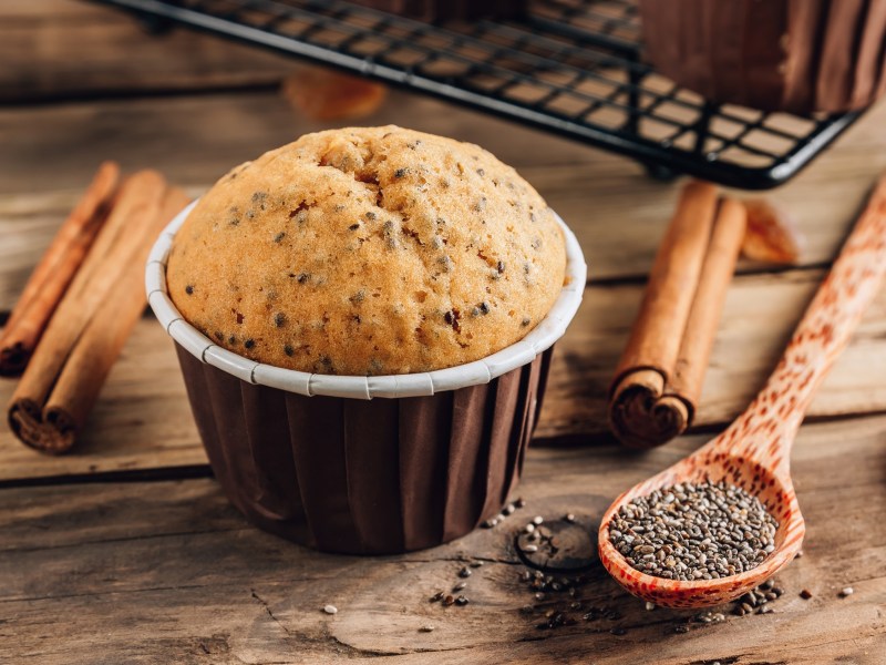 Ein Zimtmuffin. Daneben liegen ein LÃ¶ffel Chiasamen und einige Zimtstangen.