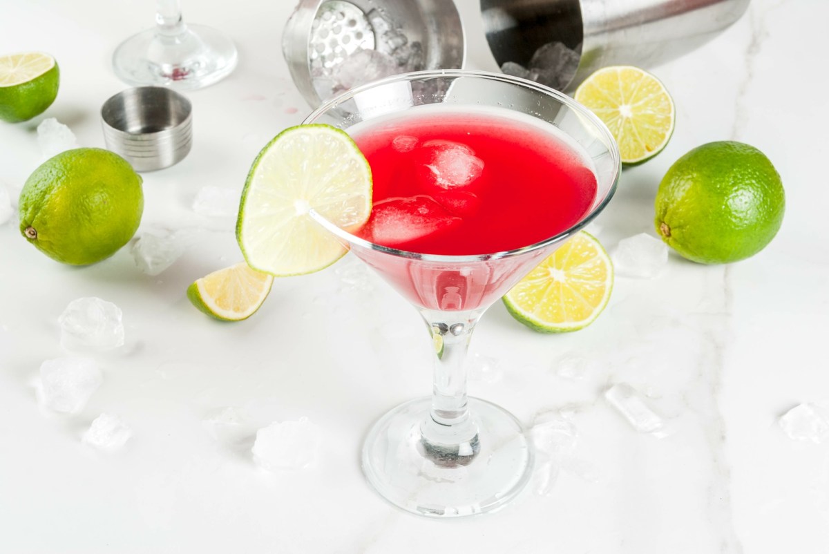 Glas alkohilfreier Cosmopolitan auf einem Tisch mit Limetten und Cocktailshaker