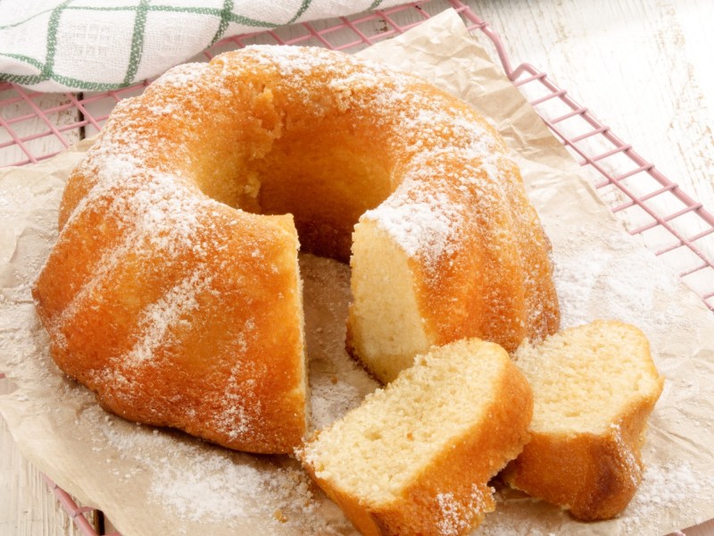 ein angeschnittener Apfelmuskuchen mit Zimt in Gugelhupfform, zwei StÃ¼cke liegen neben dem Kuchen. Nahaufnahme.