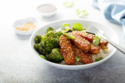 Brokkoli-Tempeh-Bowl mit geröstetem Brokkoli uns Reis,garniert mit Sesam. Eine Gabel liegt in der Schale.