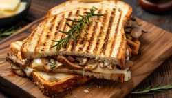 Gegrilltes Champignon-Käse-Sandwich mit Rosmarinzweig darauf auf einem Brett