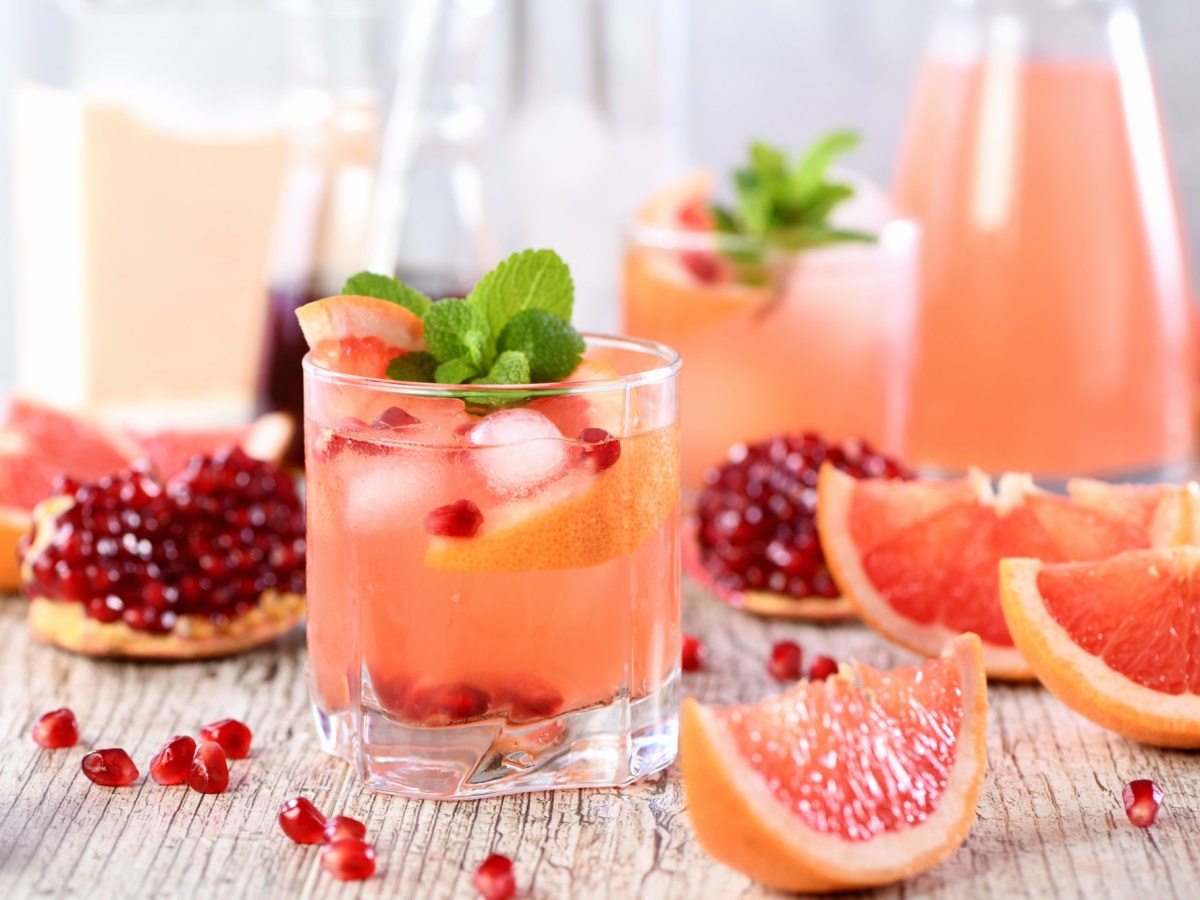 Mehere Gläser und eine Karaffe Grapefruit-Granatapfel-Mocktail, daneben liegen die Zutaten.