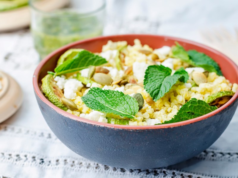 Hirsesalat mit ZiegenkÃ¤se in einer . Angerichtet mit frischen MinzblÃ¤ttern in einer schwarz-roten SchÃ¼ssel auf einem weiÃŸen Tuch.