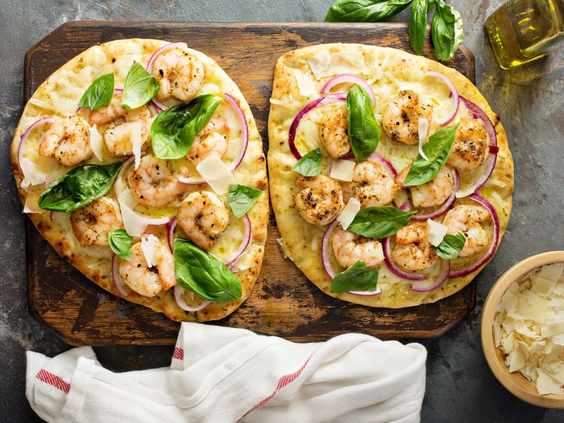 Zwei StÃ¼ck Knoblauch-Naan mit Garnelen, garniert mit Basilikum und roter Zwiebel.