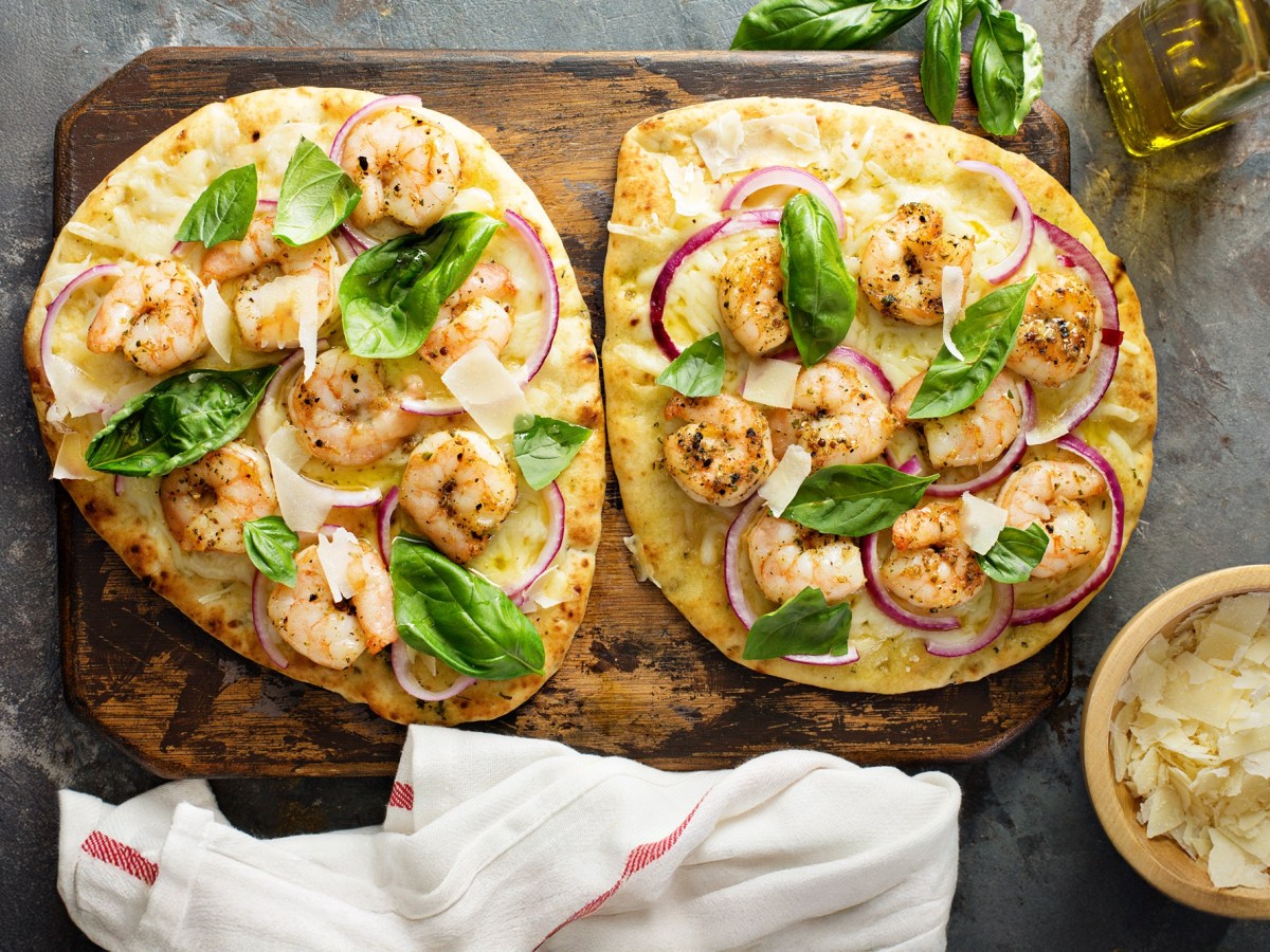 Zwei Stück Knoblauch-Naan mit Garnelen, garniert mit Basilikum und roter Zwiebel.