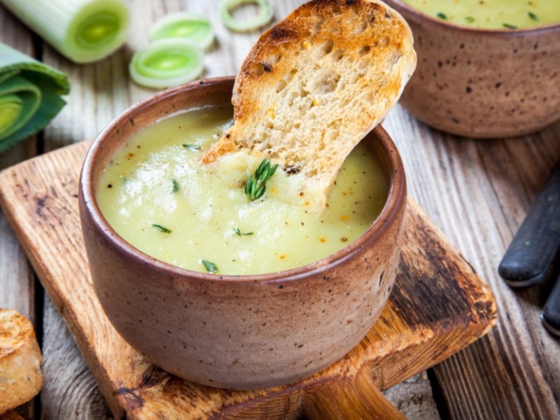 Eine Schale mit veganer Lauch-Pastinaken-Suppe, in der ein Stück kross gebackenes Brot steckt.