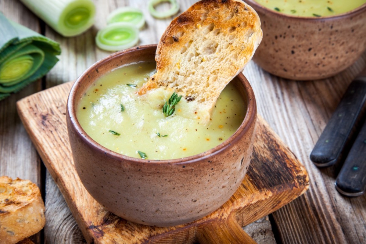 Eine Schale mit veganer Lauch-Pastinaken-Suppe, in der ein Stück kross gebackenes Brot steckt.