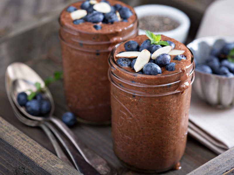 Zwei GlÃ¤ser Schoko-Chia-Pudding, garniert mit Beeren und Mandeln.