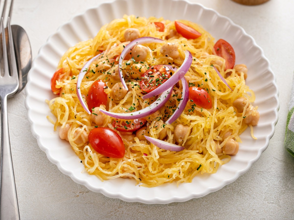 Ein Teller zubereiteter Spaghettikürbis mit Tomaten und Kichererbsen.