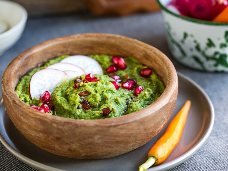 Eine SchÃ¼ssel Spinat-Hummus, serviert mit Granatapfelkernen und Radieschenscheiben.