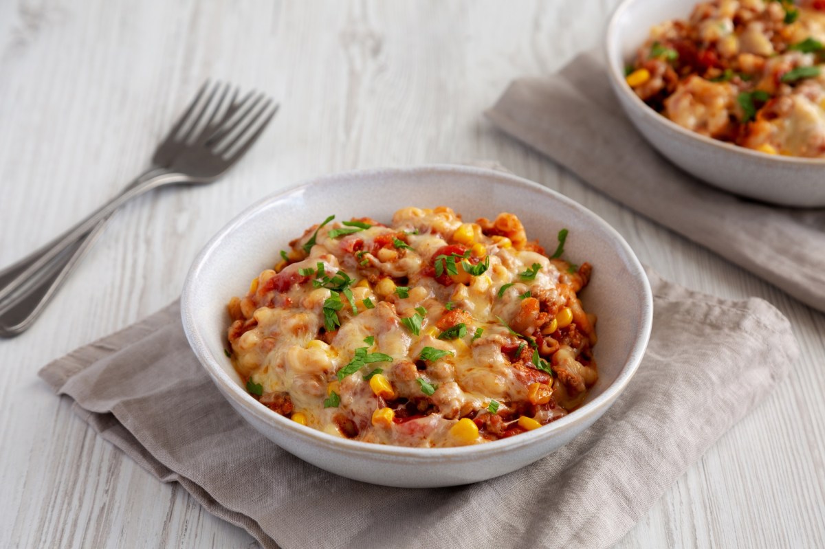 Ein weiÃŸer Teller voll mit veganer One Pot Taco Pasta, der auf einer grauen Stoffserviette steht. SchrÃ¤g links daneben liegen zwei Gabeln. In der rechten oberen Bildecke kann mit verschwommen einen weiteren Teller mit veganer One Pot Taco Pasta erkennen.