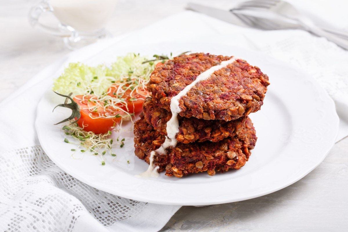 Vegane Rotkohlbratlinge mit Haferflocken liegen auf einem weiÃŸen Teller. Daneben liegt etwas Gartenkresse und eine halbierte Tomate.