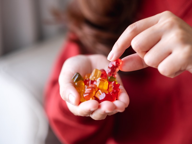 Vegane SÃ¼ÃŸigkeiten: eine Frau isst GummibÃ¤rchen aus ihrer Hand, man sieht nur ihre HÃ¤nde und ihrem OberkÃ¶rper.