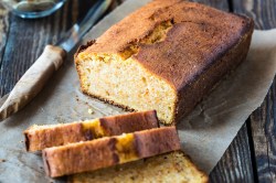 Veganer Chai-Kuchen liegt angeschnitten auf einem Stück Backpapier auf einem dunklen Holztisch.