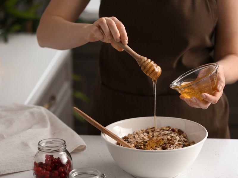 Eine Frau sÃ¼ÃŸt ihr MÃ¼sli mit veganem Honig, man sieht nur ihre HÃ¤nde und ihren OberkÃ¶rper.