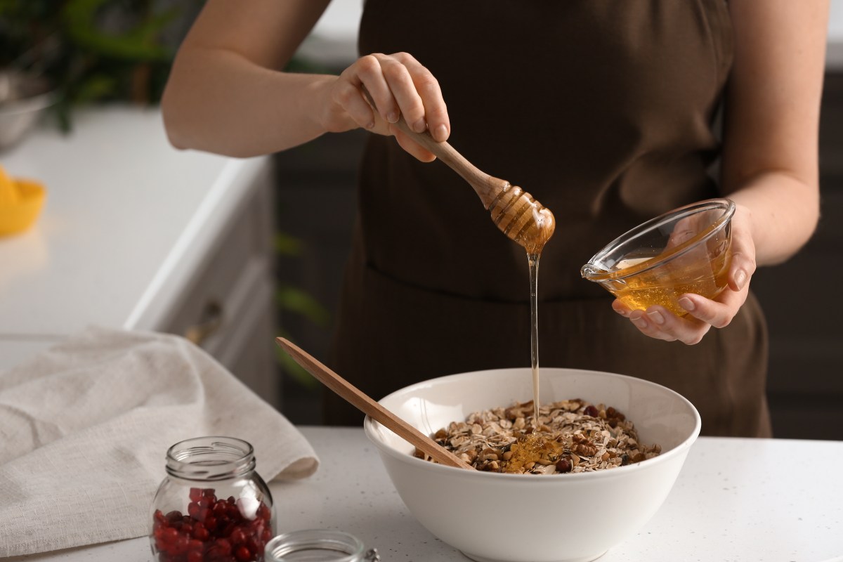 Eine Frau sÃ¼ÃŸt ihr MÃ¼sli mit veganem Honig, man sieht nur ihre HÃ¤nde und ihren OberkÃ¶rper.