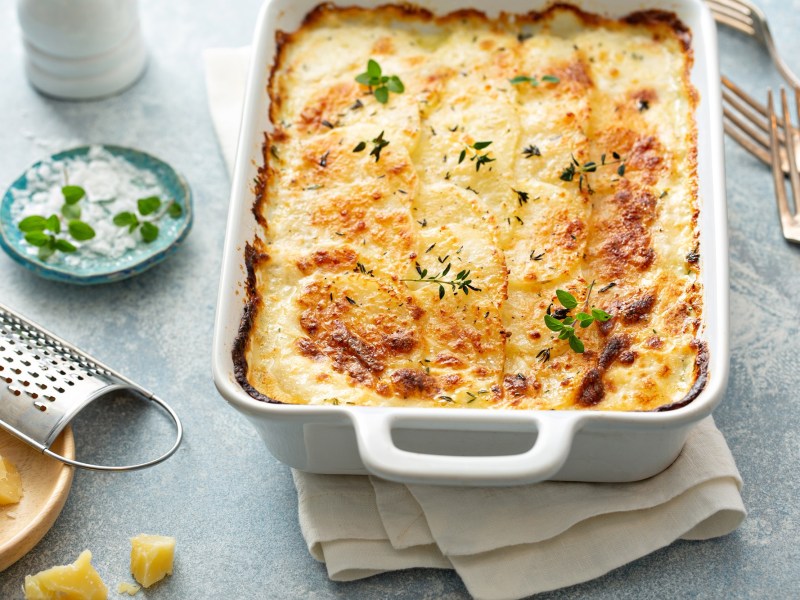 Veganes Kartoffelgratin in weiÃŸer Auflaufform, mit KrÃ¤utern bestreut, drumherum einige Zutaten.