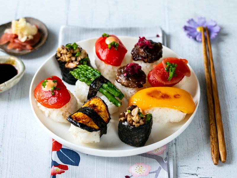 Farbenfrohes, veganes Sushi auf einem weiÃŸen Teller. Daneben liegen EssstÃ¤bchen.