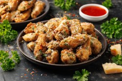 Ein Teller Knoblauch-Parmesan-Hühnchen aus dem Airfryer, daneben eine Schale mit roter Salsa und Parmesanstücke.