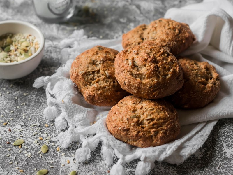 Mehrere Vollkornbrötchen mit Saaten auf einem hellen Tuch.