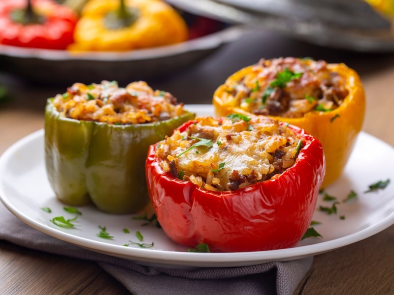 Drei Mal gefüllte Paprika mit Reis und Hackfleisch auf einem weißen Teller.