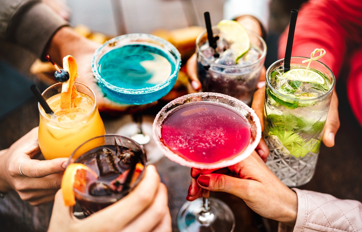 Verschiedene Cocktails, die von Händen zum Anstoßen zusammengehalten werden.