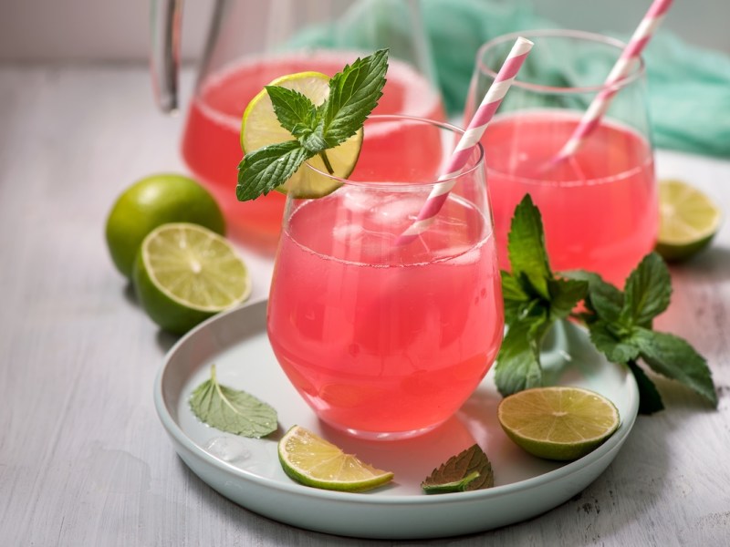 3 Gläser Rhabarber-Holunder-Spritz mit Strohhalmen, garniert mit Minze und Limetten.